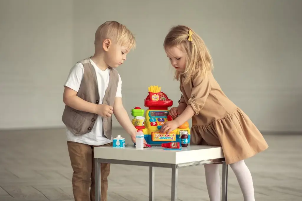 Two children engaging with a toy cash register at a table, capturing playful innocence.